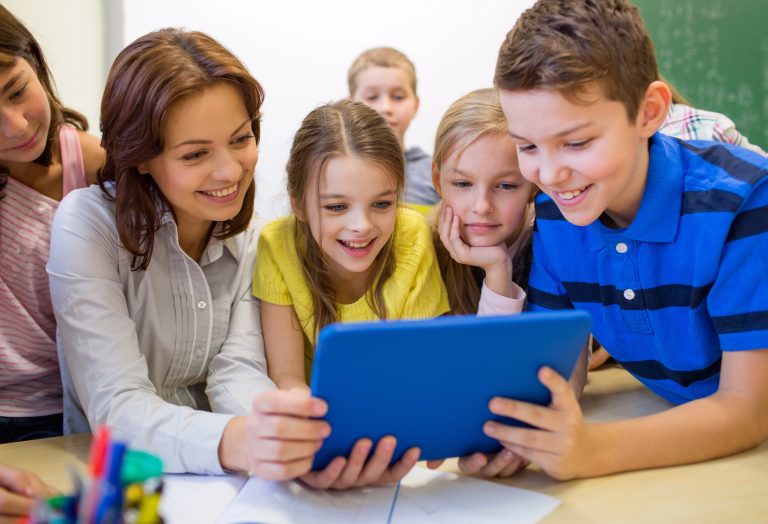 A coach working with a group of elementary-aged students gathered around a tablet in a classroom setting